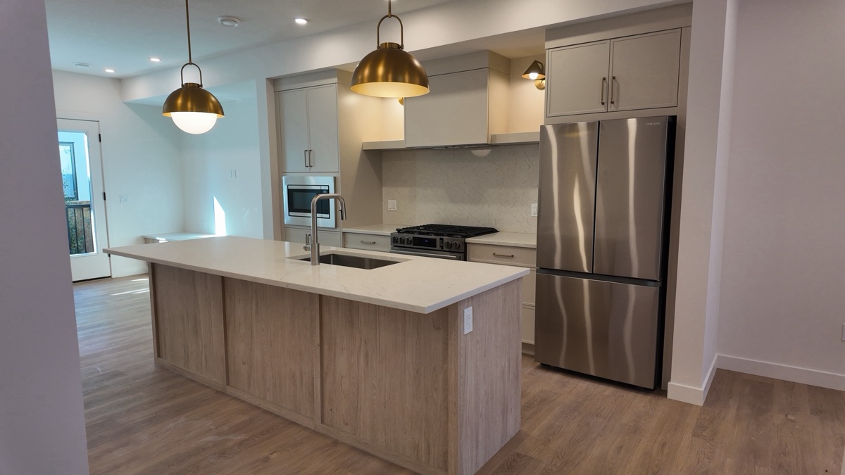 Townhouse kitchen with quartz island, gas range and stainless French-door fridge.